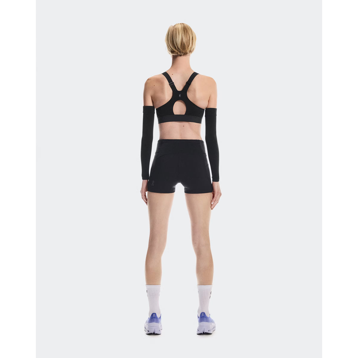 Women's On Performance Bra Black full body back view on female runner showing mesh racerback inserts for breathability and adjustable straps with back-positioned adjusters for comfort
