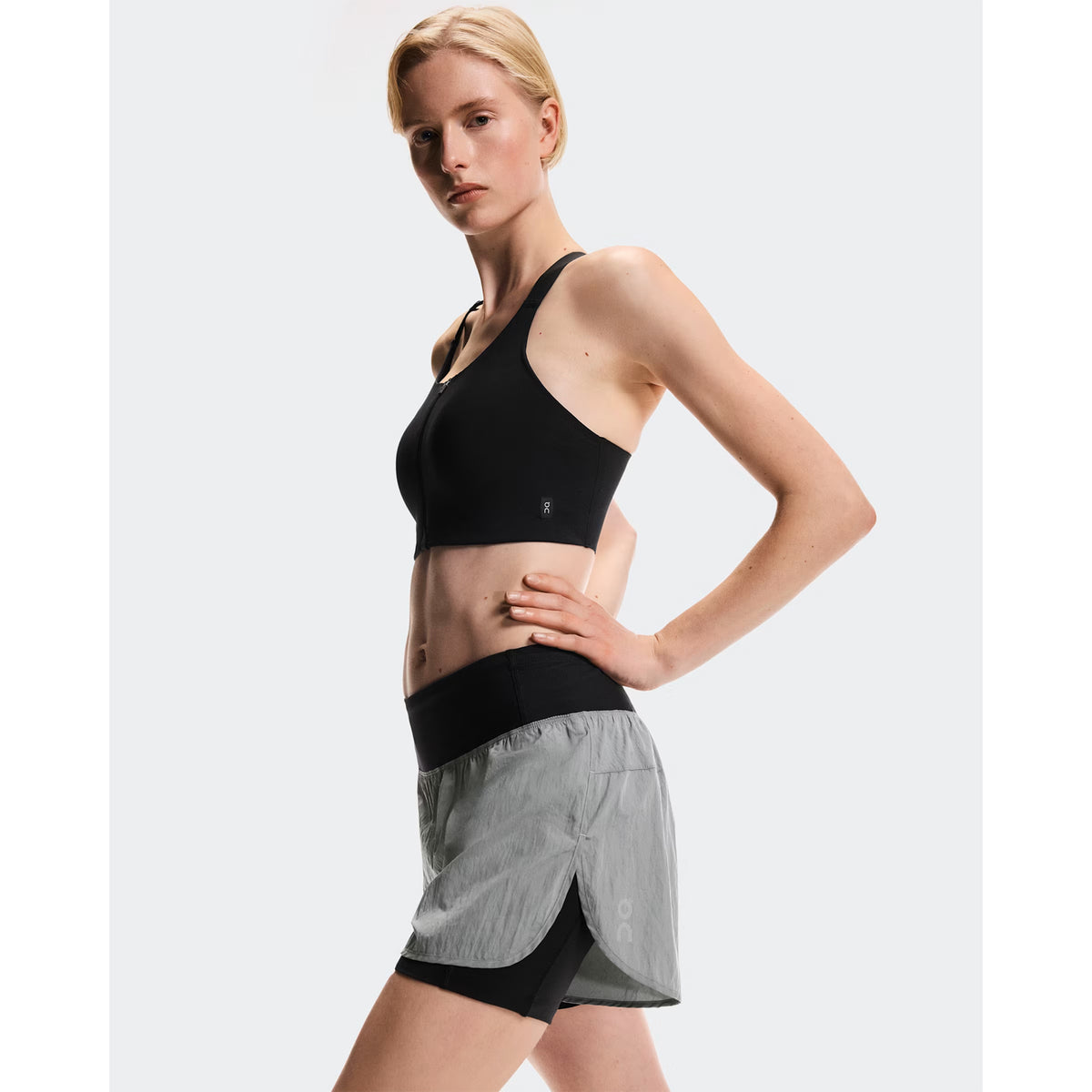 Women's On Performance Volt Shorts Glacier side view on female runner showing dual-layer construction with windproof iridescent outer, four-way stretch inner tights and moisture-wicking On DryTec technology paired with sports Performance Bra
