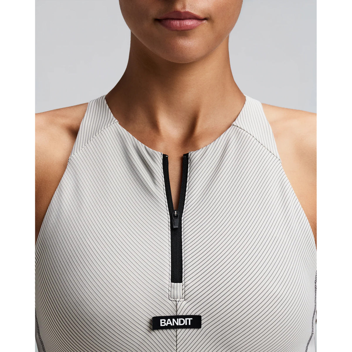 Women's Bandit Striped Cadence Zip Front Race Crop Plaster Slate close-up of front showing custom-branded zip with Striped Cadence ribbed compression and silicone front patch detail
