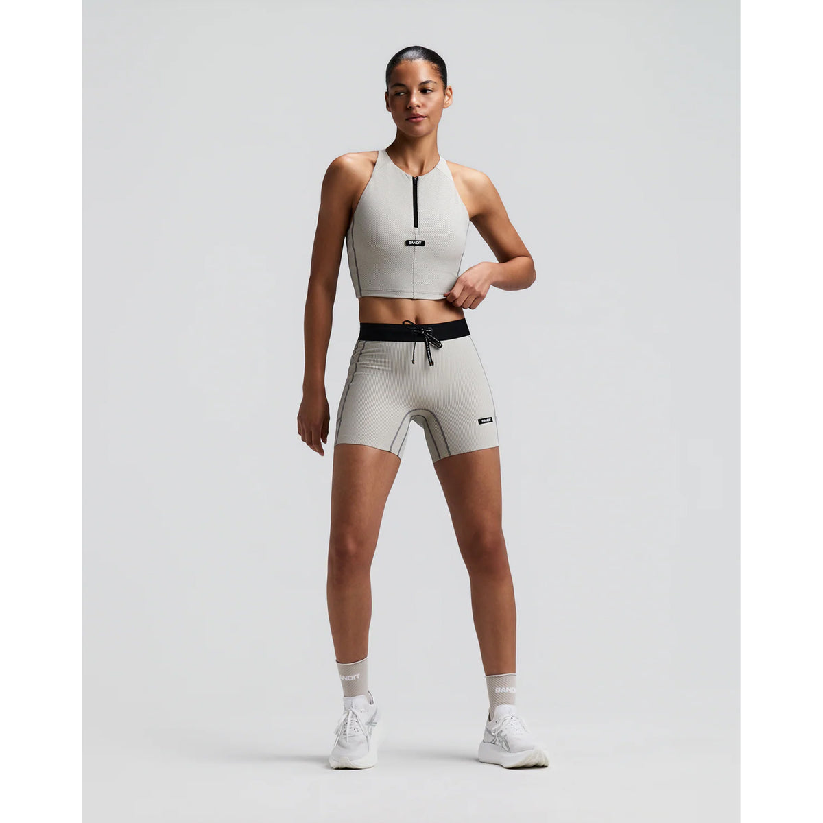 Women's Bandit Striped Cadence Zip Front Race Crop Plaster Slate front full body view on female runner showing halter fit with zip front, Striped Cadence ribbed compression and seven-pocket system for road running and racing