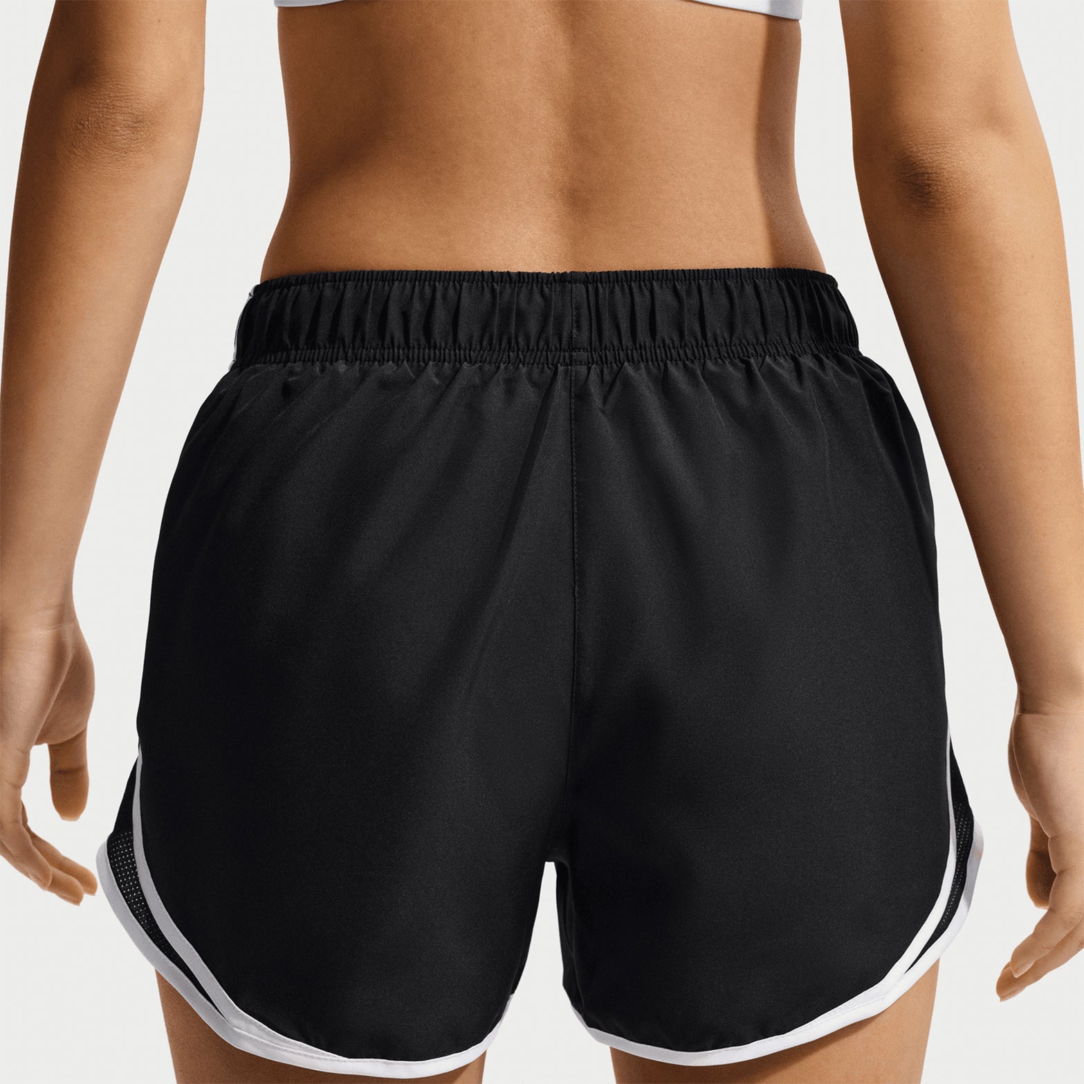 A person stands facing away, wearing a gray sports bra and Nike Women’s Tempo Dri-FIT Mid Rise Running Shorts in Black/Black/White—featuring moisture-wicking Dri-FIT technology—against a plain light background.