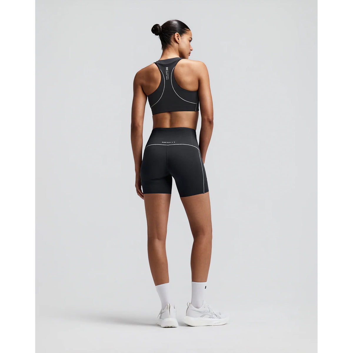 Women's Bandit Vanisher Pop Stitch Arco Run Bra Anthracite back full body view on female runner showing waterproof back phone pocket with reflective branding and Vanisher compression for comfortable running