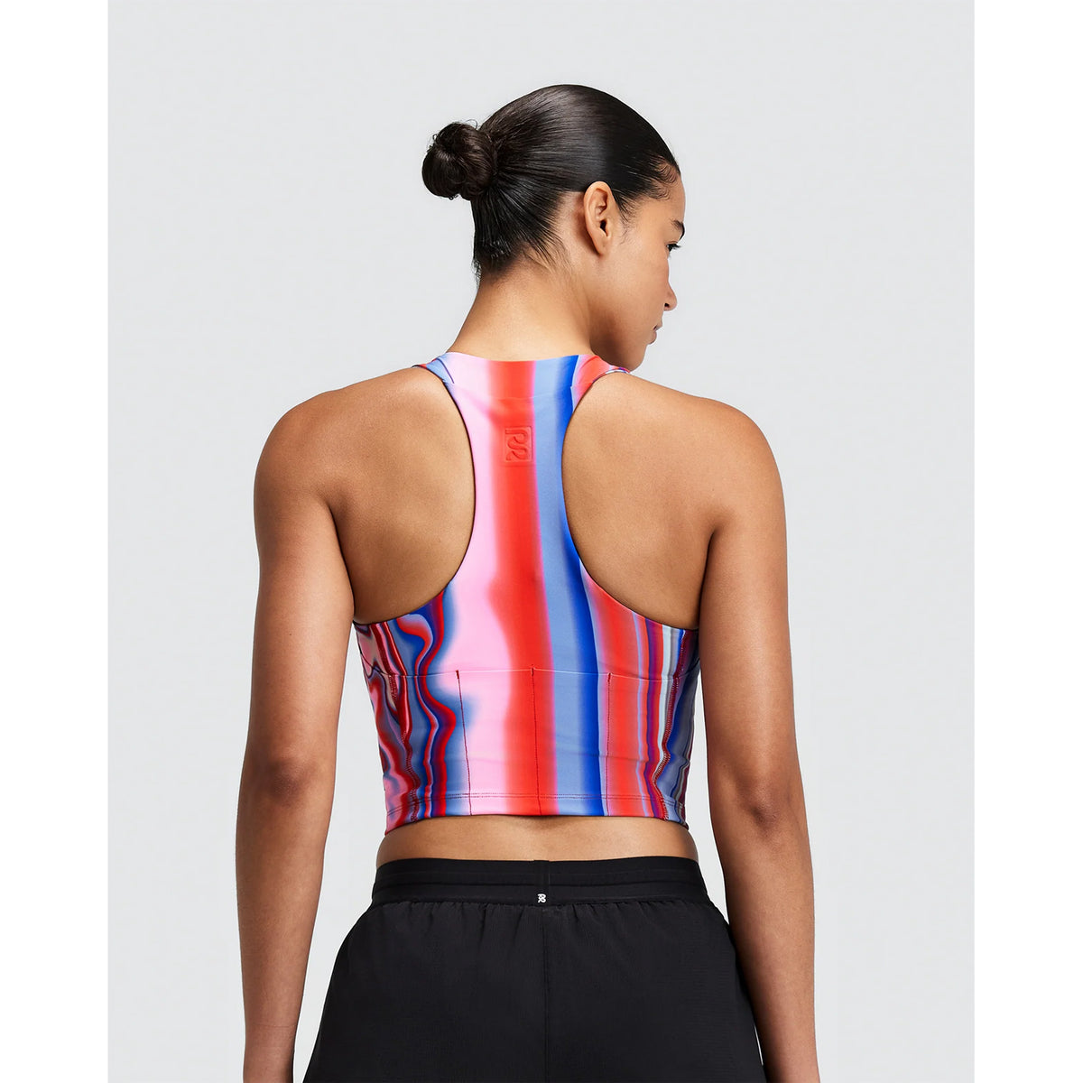 Back view of a person wearing a Bandit Women’s Vanisher Race Crop Melted Stripe Gradient in red, pink, and blue stripes with black shorts.