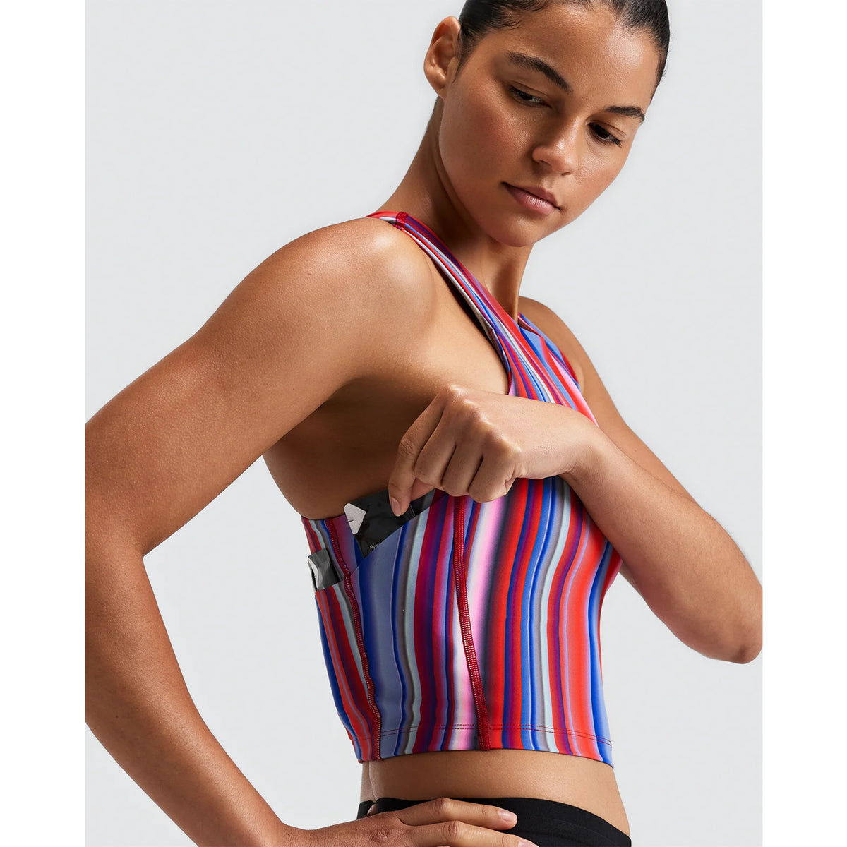 A person wearing a striped, multi-colored Women’s Vanisher Race Crop Melted Stripe Gradient with a side pocket, placing a small item into the pocket.