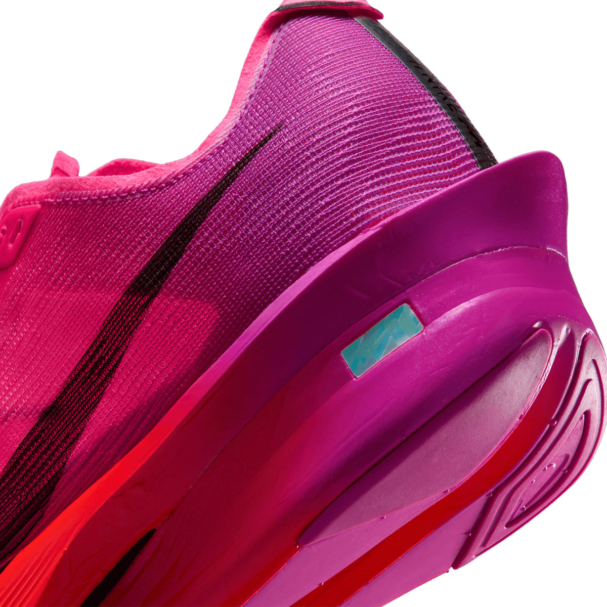 Close-up of a pink running shoe with a black swoosh logo, detailed texture, and a visible blue label near the heel on the outsole.