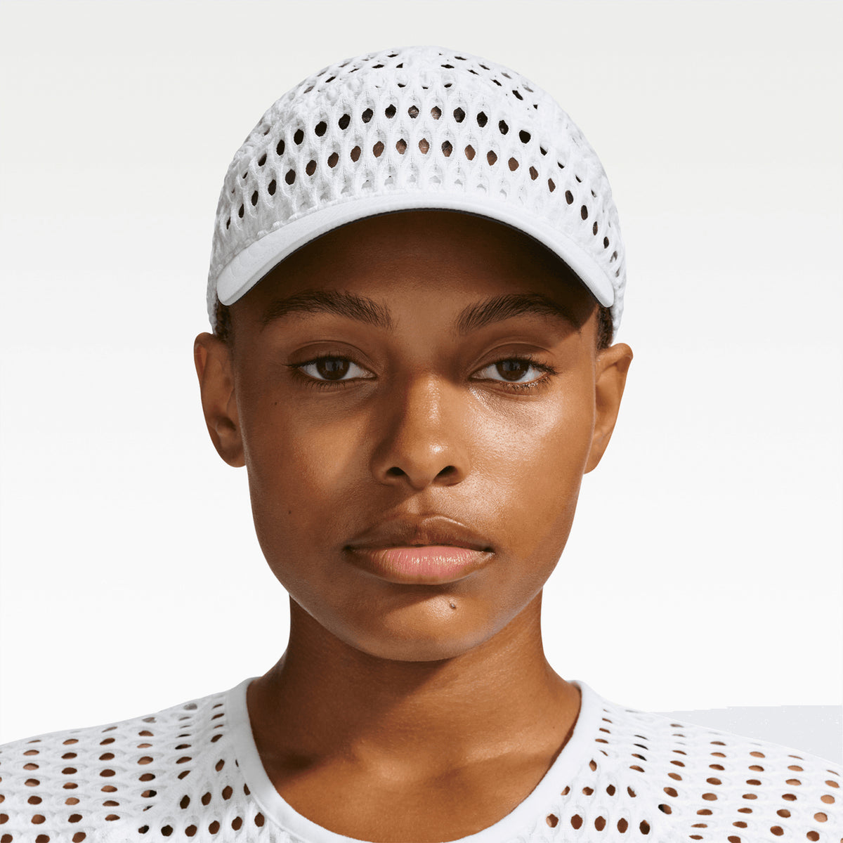 A person wears a white Nike ACG Radical AirFlow Fly Cap featuring an all-over perforated mesh pattern.