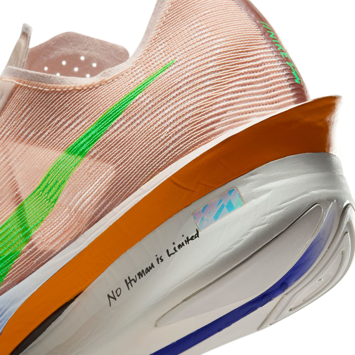 Close-up of a running shoe with a green swoosh, orange midsole, and the phrase No Human is Limited printed on the white part above the sole.
