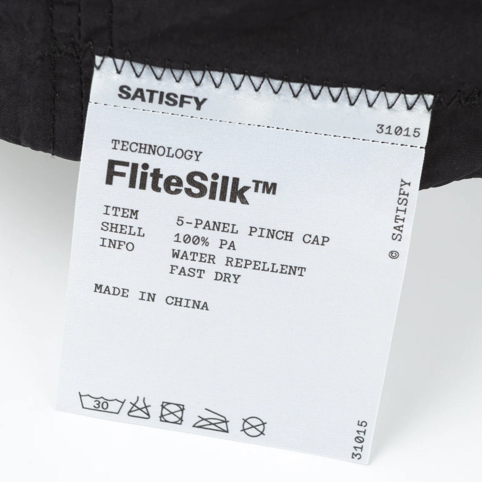 Satisfy FliteSilk™ 5 Panel Pinch Cap in Black Eagle — closeup showing fully detachable exterior care label on black FliteSilk™ Italian nylon fabric