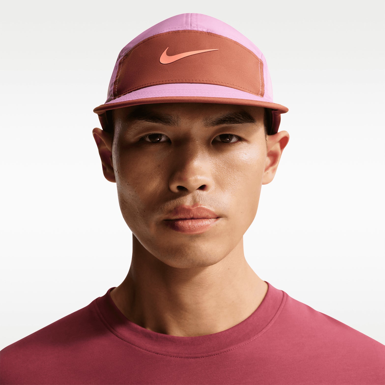 Nike Fly Unstructured Swoosh Cap Light Magenta Dusty Peach Anthracite Orange Frost on male model showing unstructured fit with curved bill and lightweight breathable four-way stretch fabric for running, gym and trail activities