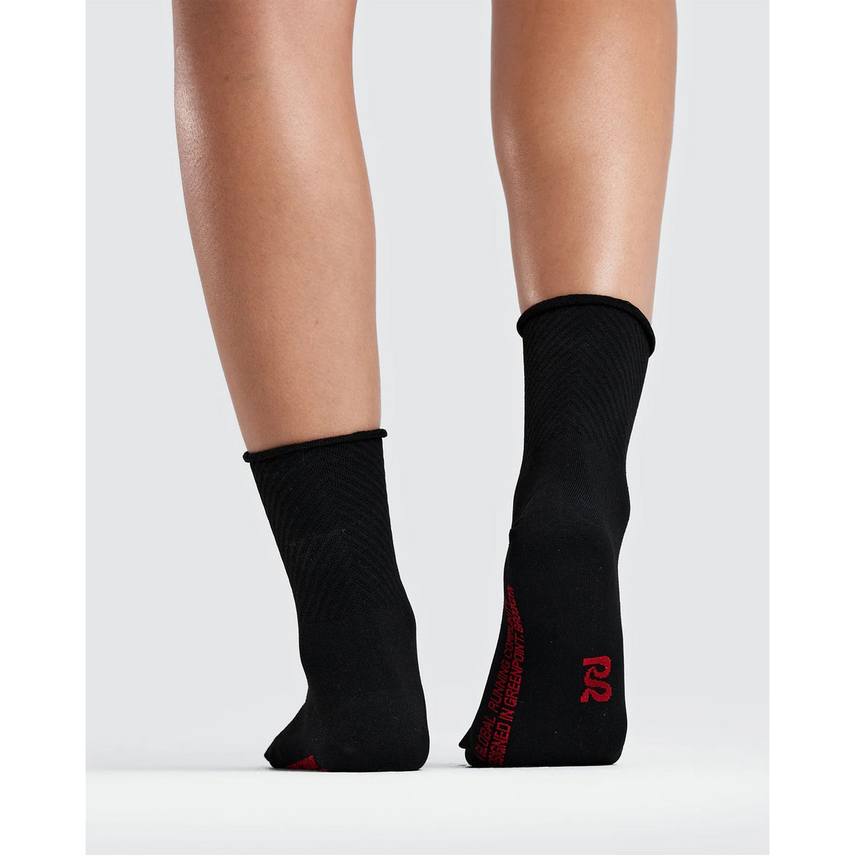 A person wearing black Bandit Lite Run Ribbed 2 Pack Quarter Socks featuring red lettering and a logo on the heel.