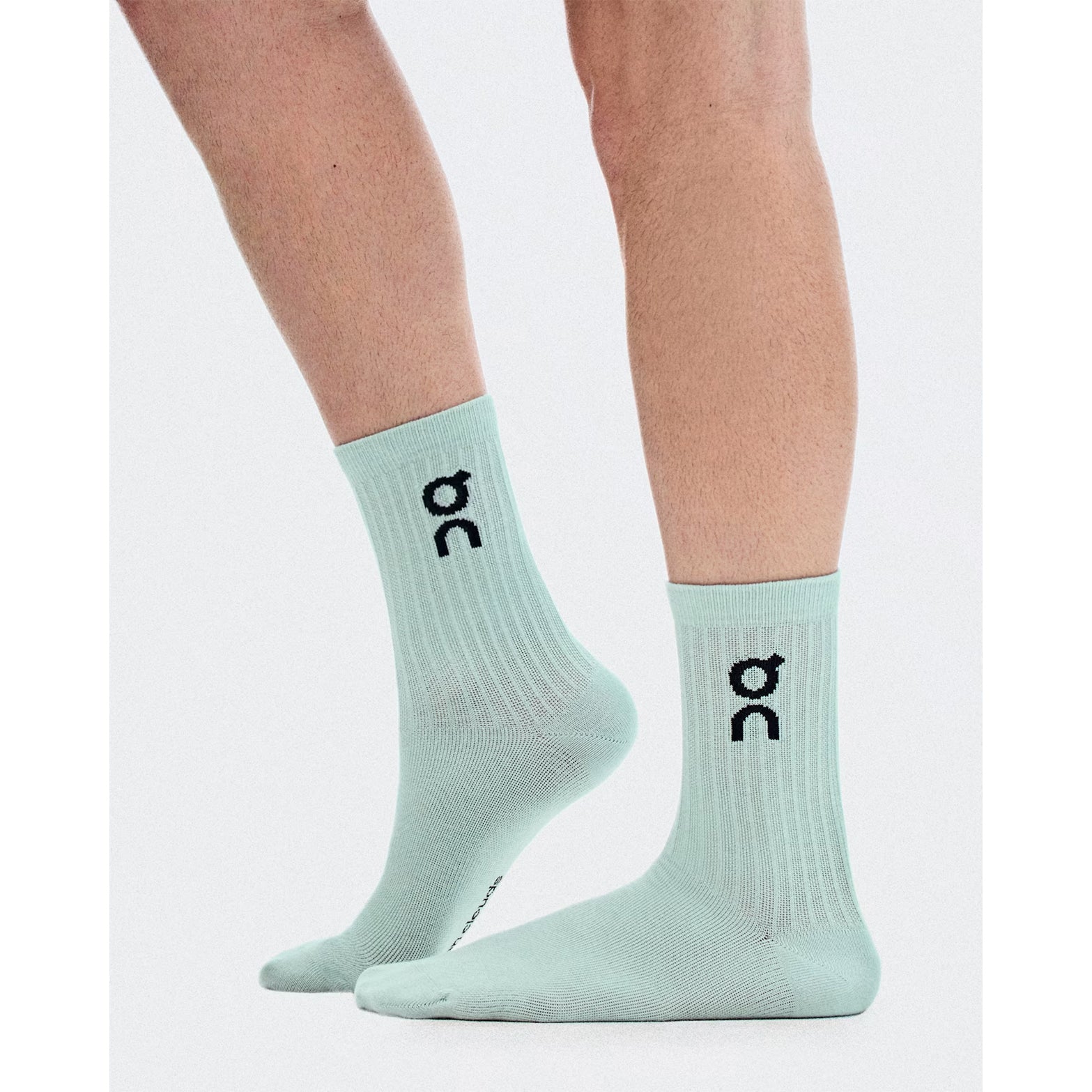 A person wears the On Logo Socks High 3 Pack in Brook / Storm, featuring a black On logo, while standing on a white background. These versatile running socks offer all-day comfort and dependable arch support.