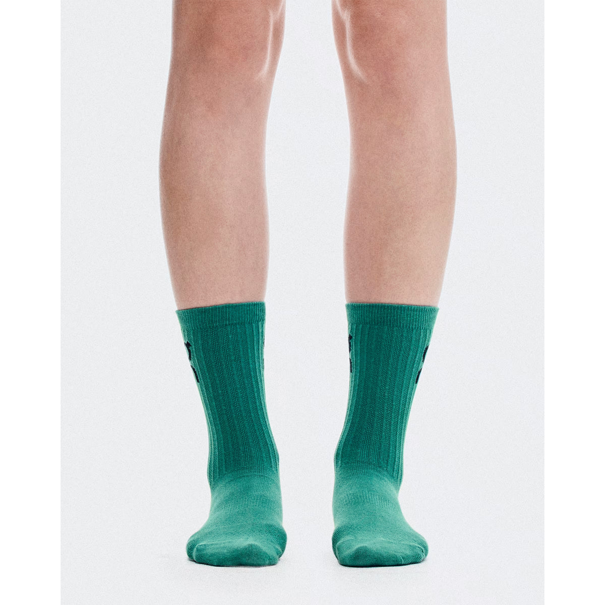 A pair of legs wearing On’s Logo Socks High 3 Pack Brook / Storm are shown from the knees down, standing on a white background.