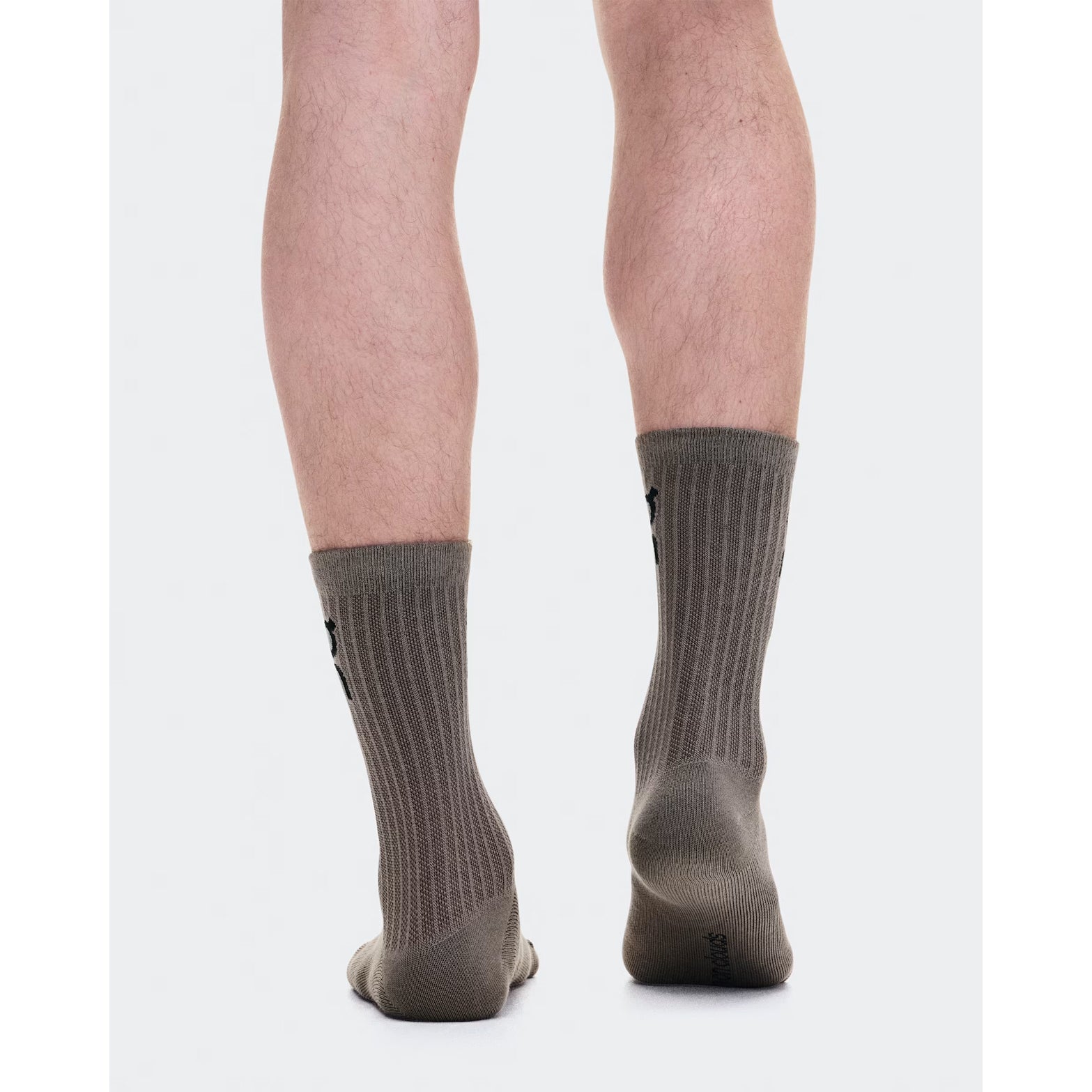 Back view of a person standing on tiptoes, wearing On Logo Socks High in the Hare / Brume colorway—a ribbed, mid-calf style designed for all-day comfort. The plain white background highlights the legs and socks, with feet close together and slightly turned inward.