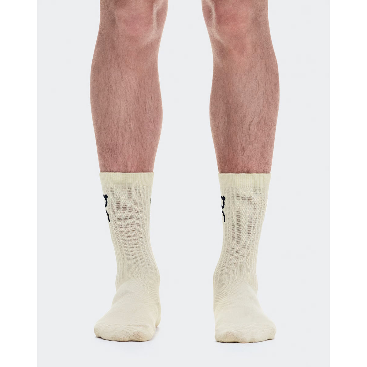 A person stands with feet together, wearing On’s Logo Socks High in the Hare / Brume colorway—off-white ribbed all-day comfort socks featuring a small black logo on the back—against a white background.