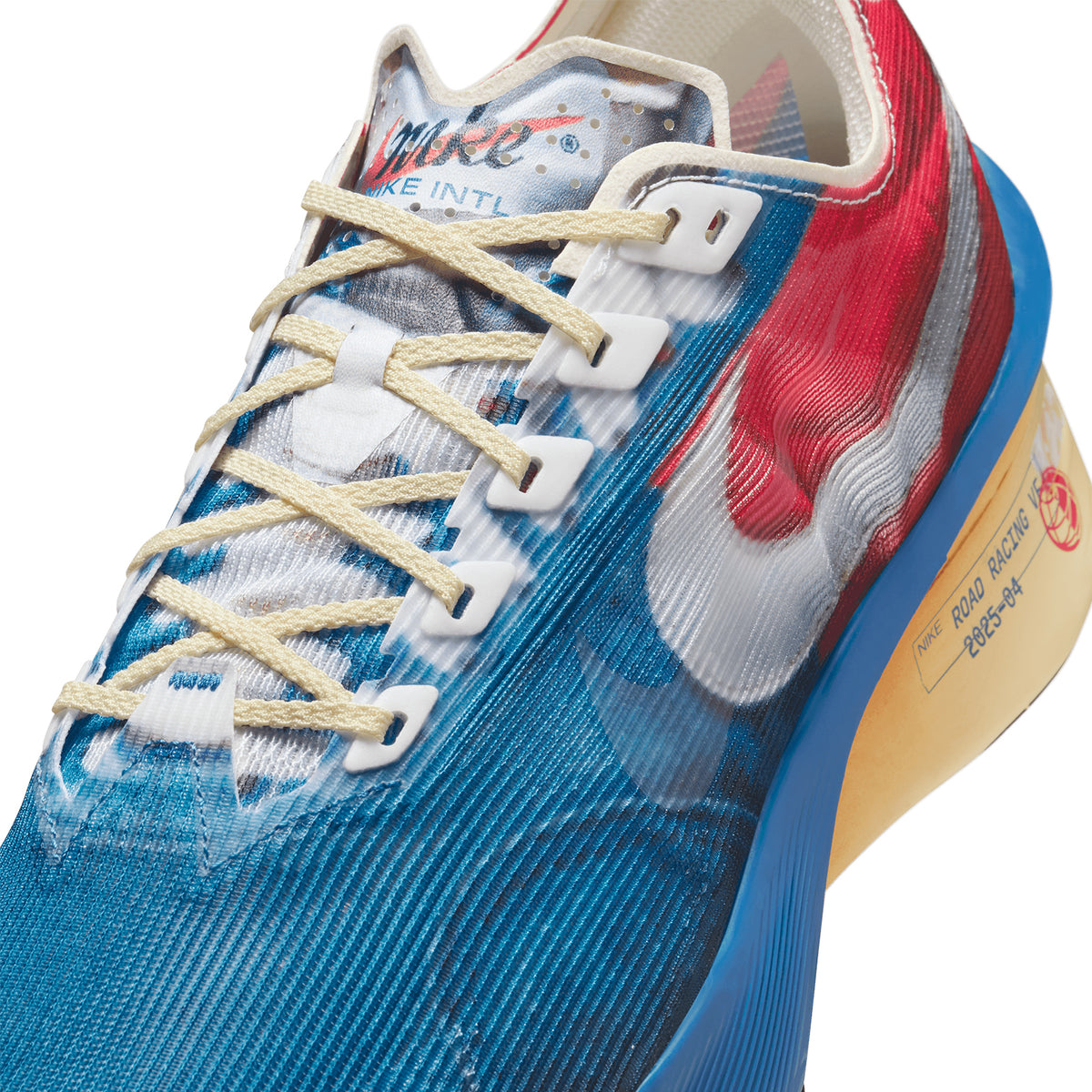 Close-up of a colorful Nike running shoe with blue, red, and white details, beige laces, a white Nike swoosh, and a yellow sole that has text printed on it.