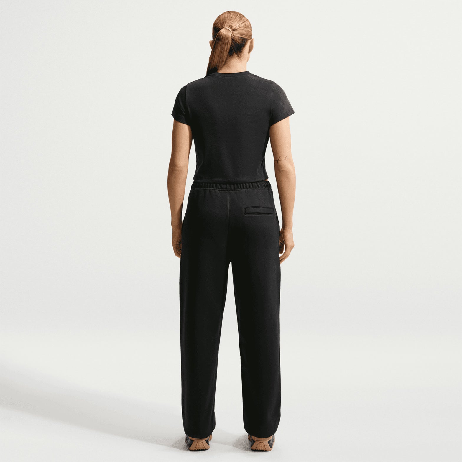 Nike ACG Tuff Fleece trousers in Black / Summit White — back view worn on female model showing black heavyweight fleece, elastic cuff detail and snap secure back pocket storage