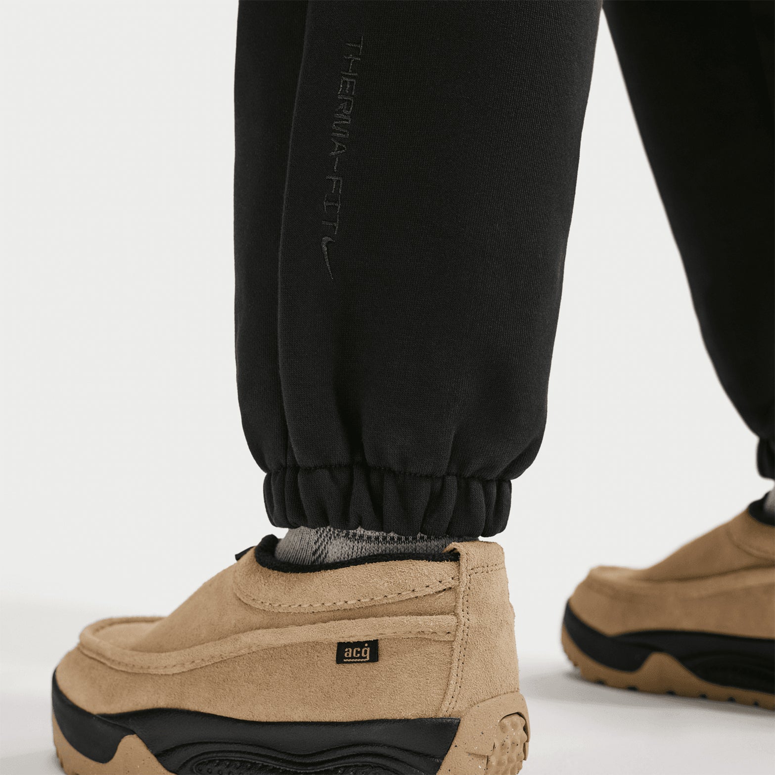Nike ACG Tuff Fleece trousers in Black / Summit White — full body view worn on male model showing black heavyweight fleece with summit white detailing, comfortable fit and Therma-FIT warmth construction