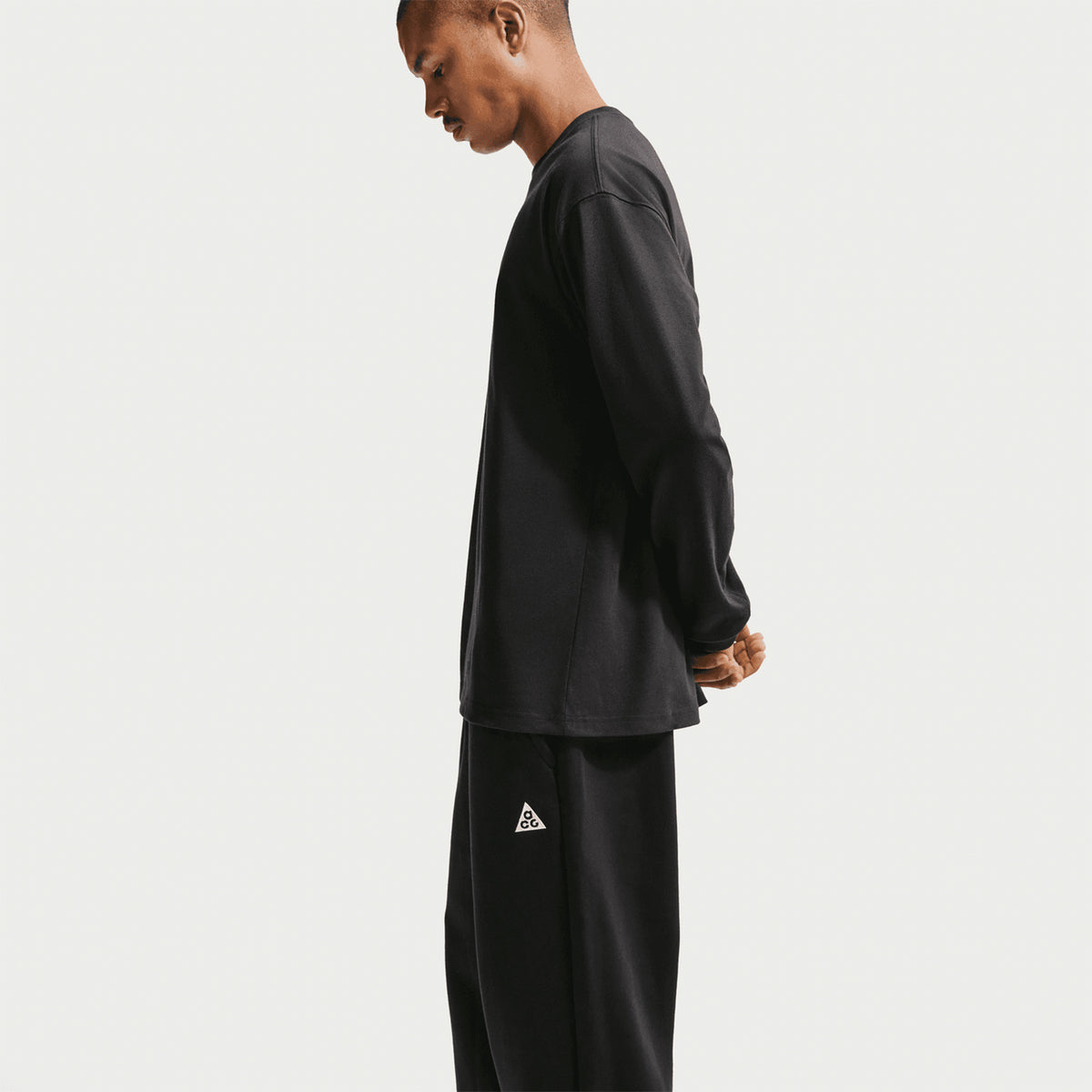 Nike ACG Tuff Fleece trousers in Black / Summit White — side view worn on male model showing black Therma-FIT fleece construction, locker loop and water-repellent finish for cold weather durability