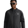 Men's Nike ACG Rope de Dope Jacket Black Summit White front view on male runner showing Therma-FIT ADV heat-regulating construction with bungee drawcord hem and multiple pockets for cold weather outdoor use