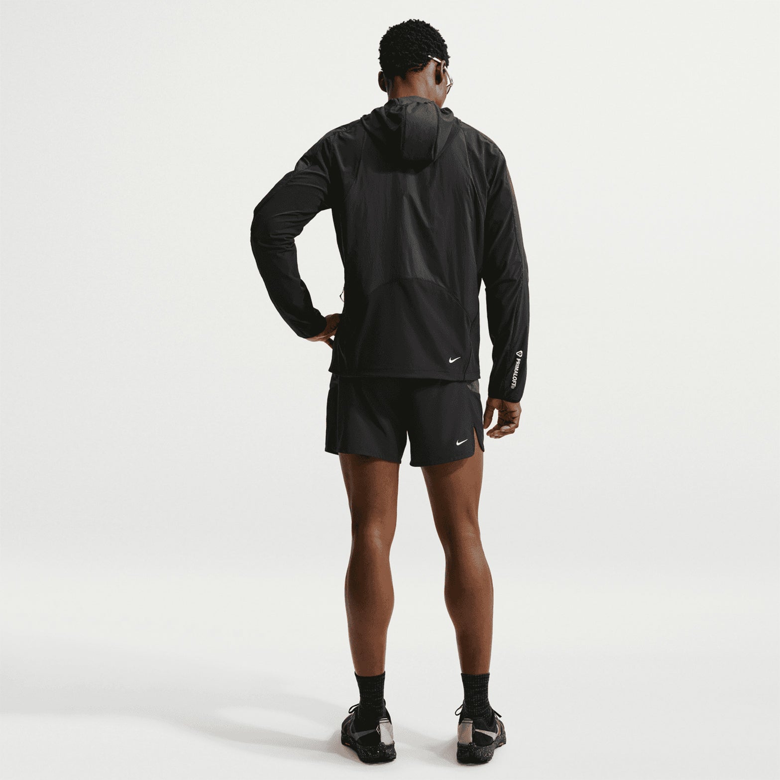 Men's Nike ACG Rope de Dope Jacket Black Summit White full body back view on male runner showing ripstop fabric with reflective details, stretch-woven panels and bungee hem for durable packable cold weather trail running
