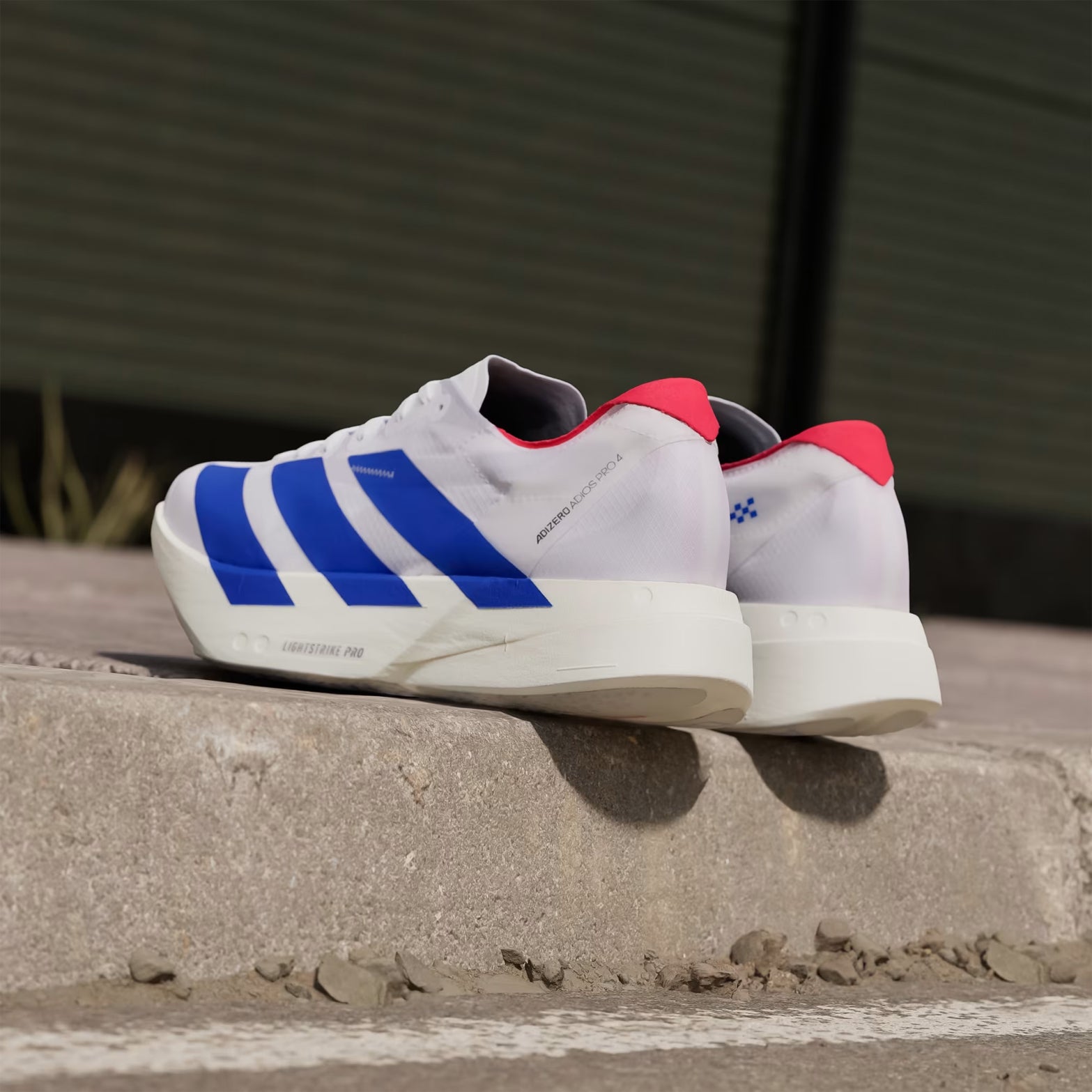 Men's adidas Adizero Adios Pro 4 Running Shoes White Blue Red angled heel view showing double-layer LIGHTSTRIKE PRO cushioning stack and carbon ENERGYRODS 2.0