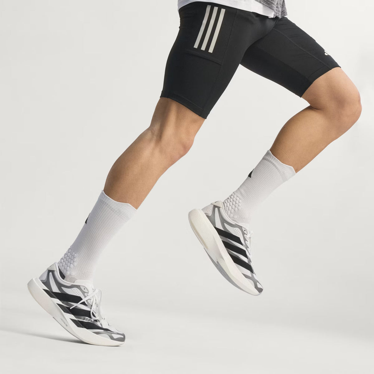 adidas Adizero EVO SL EXO men's running shoe in Cloud White / Core Black / Iron Metallic — side view worn in motion showing cloud white woven shell upper with core black exoskeleton overlays, oversized iron metallic 3-Stripes and LightstrikePro midsole profile at pace