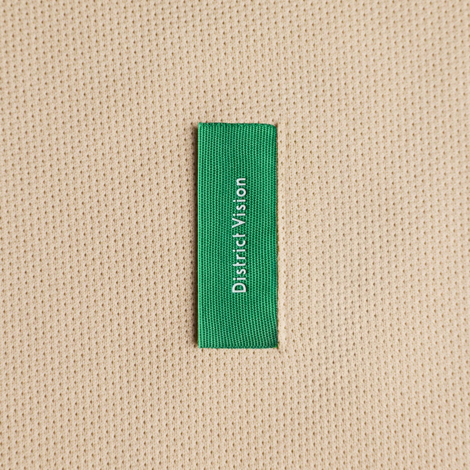 District Vision Short Sleeve Boxy Training Tee Beige close-up of custom woven label at lower right rib with barely-there feel construction