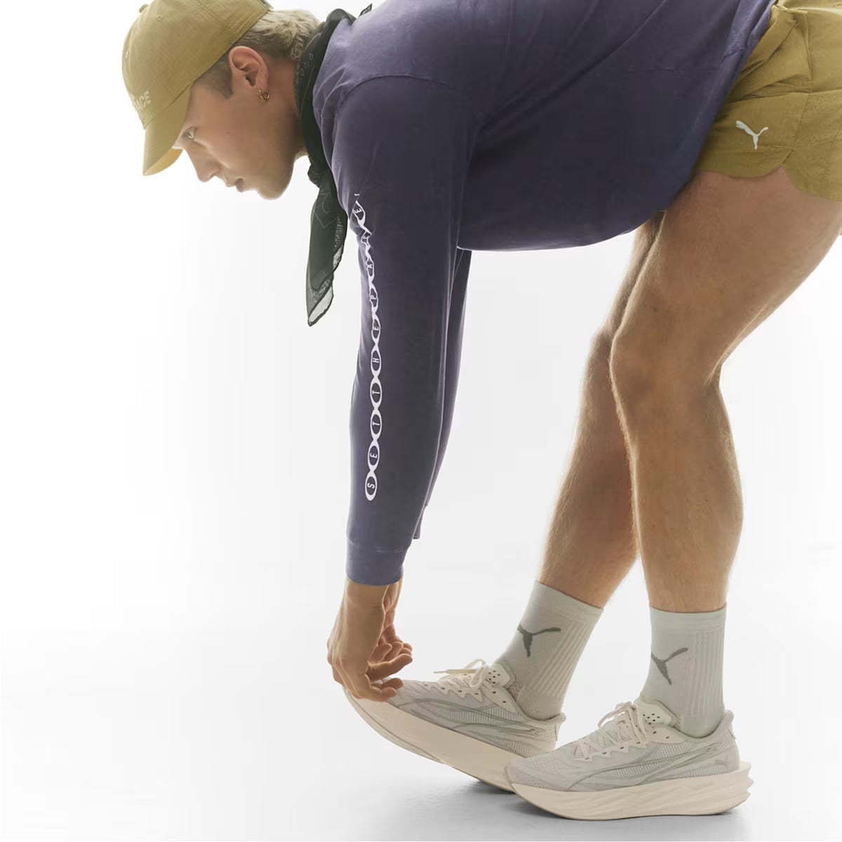 A person in a cap, purple long-sleeve shirt, khaki shorts, and white sneakers stretches downward, touching their toes against a light background.