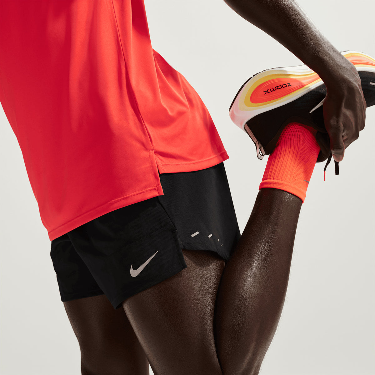 Men's Nike Dri-FIT Stride 5 Inch Shorts Black worn by male runner stretching showing shallow rise for unrestricted leg movement, standard fit and lightweight woven fabric