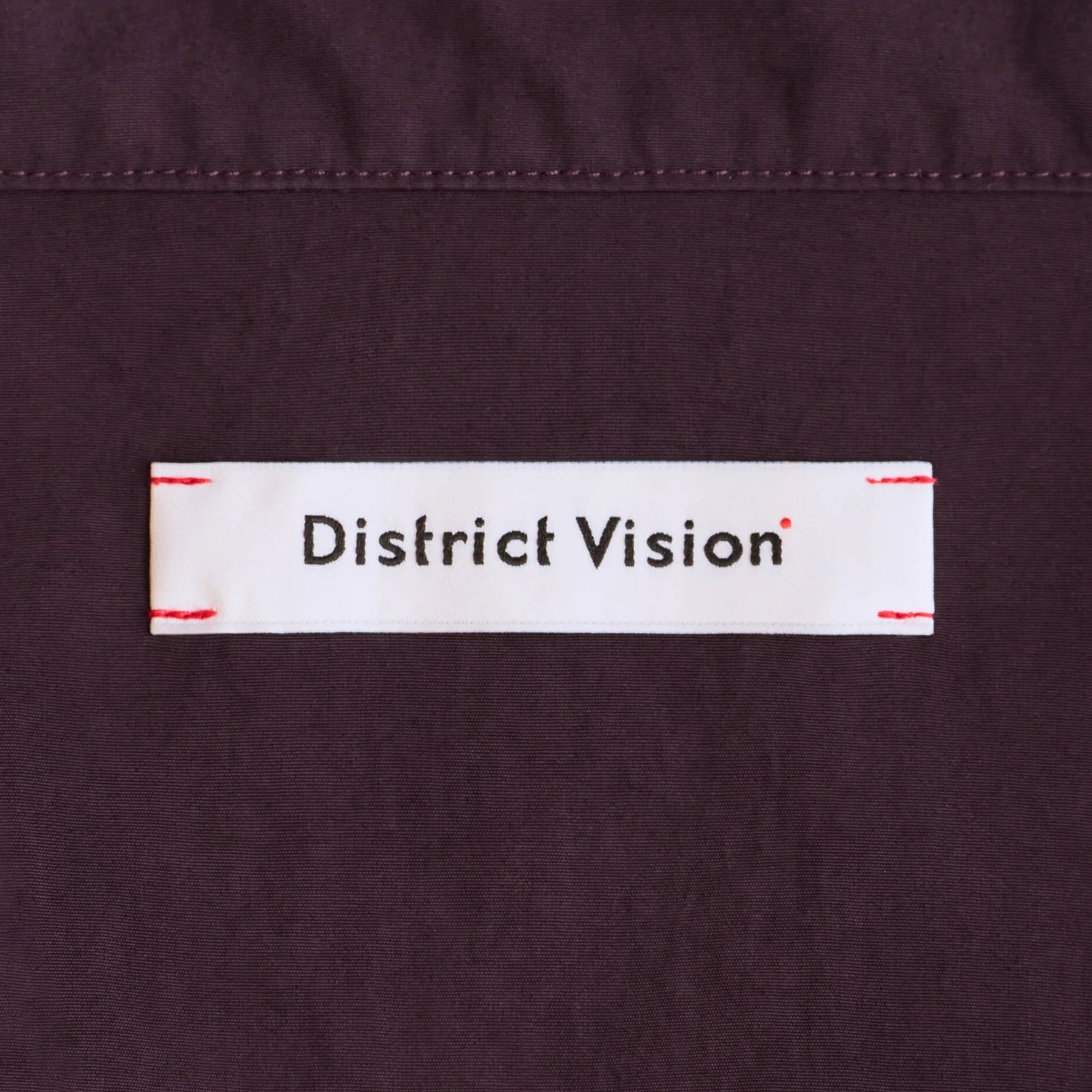 District Vision Men's Half Zip Nylon Windbreaker Blackberry close-up of custom woven label at shoulder functioning as integrated eyewear storage for securing sunglasses