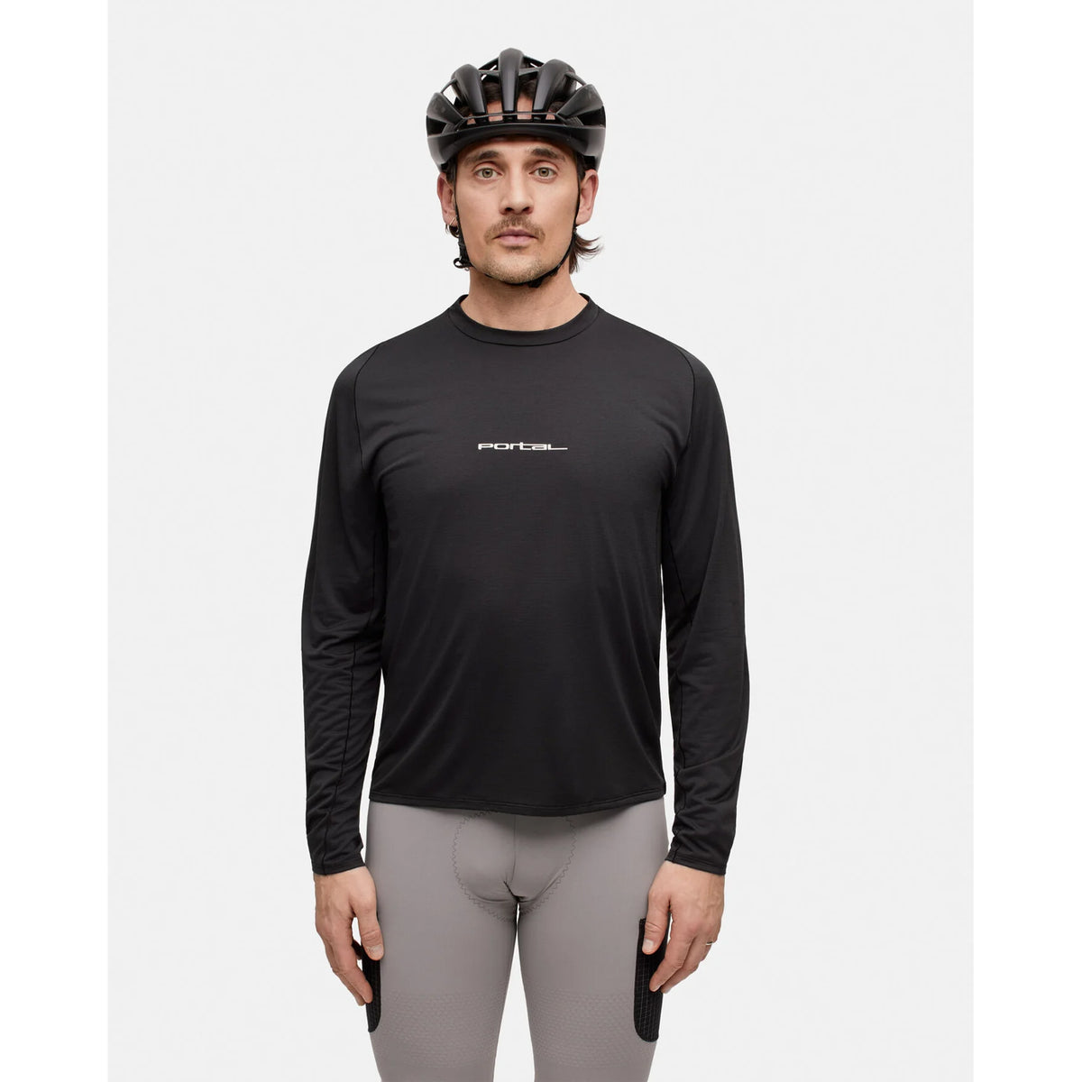 A man wearing a black cycling helmet, Portal’s Men’s Lateral Peak Long Sleeve Top Black Beauty—a moisture-wicking black shirt made from Japanese technical fabric with FORTE text—and gray cycling shorts stands facing forward against a plain white background.