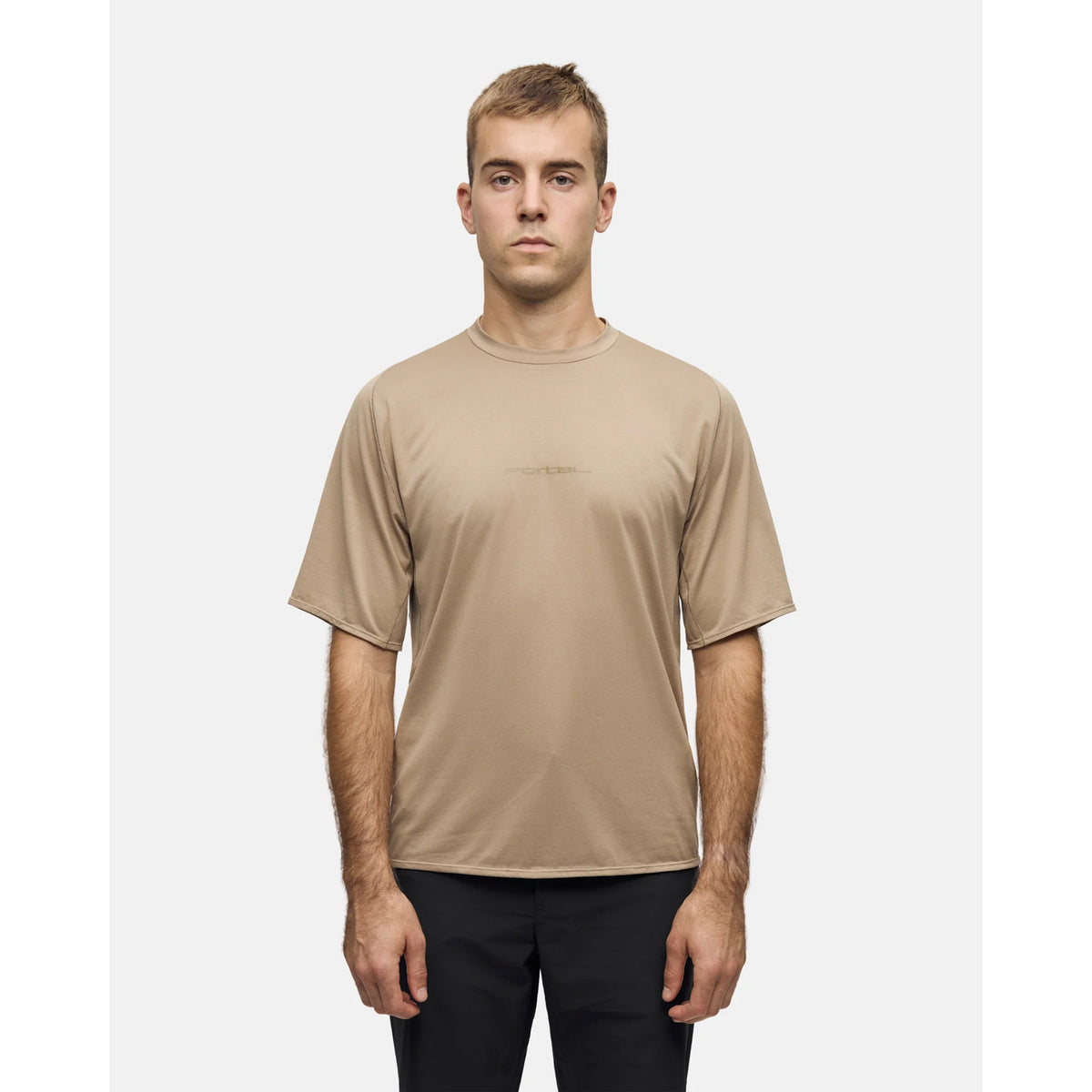A man wearing a tan, moisture-wicking, short-sleeved Portal Men’s Lateral Peak Tee Greige with a subtle logo across the chest.