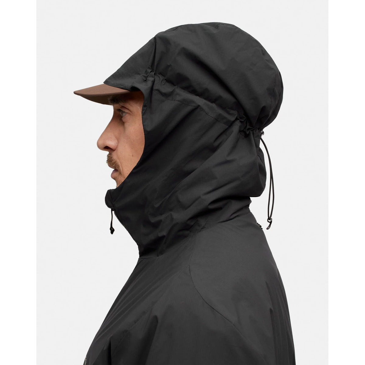 Profile view of a person wearing a Black Beauty Men’s Level Alpha Jacket with a hooded design and a brown brim.