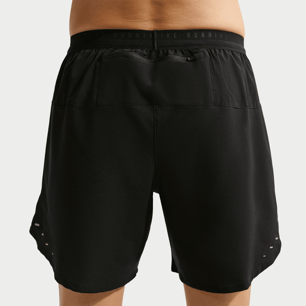 Rear view of a person wearing Nike Men’s Stride Dri-FIT 7 Inch Running Shorts in black, featuring an elastic waistband, perforated ventilation on the lower sides, and a zippered pocket designed to securely hold a phone.