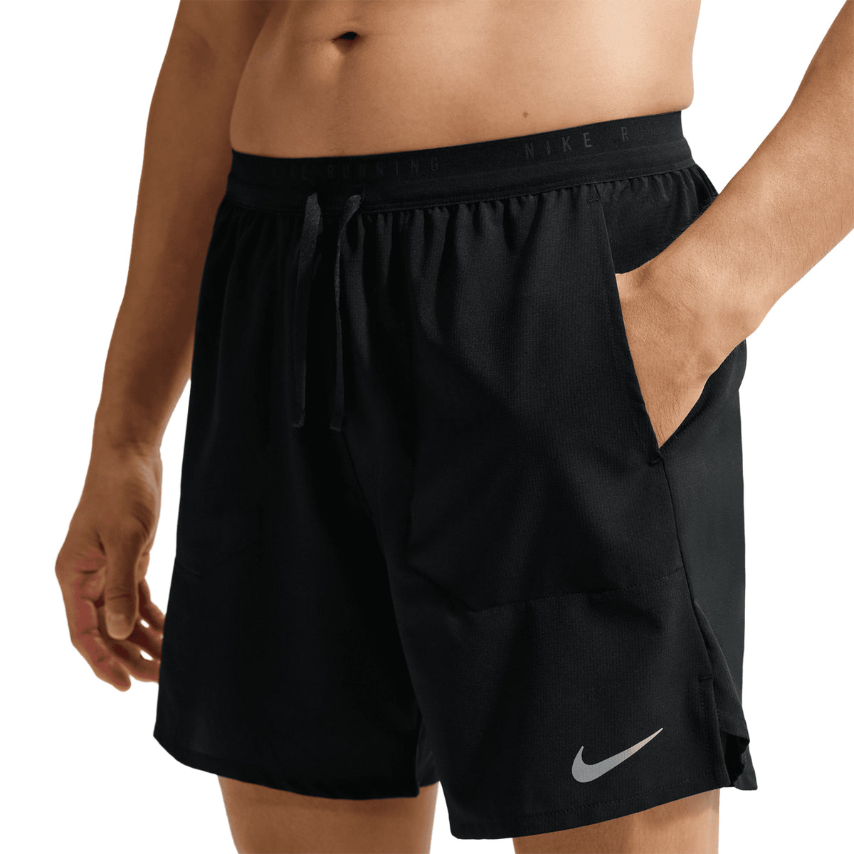 A person wearing Nike Men’s Stride Dri-FIT 7 Inch Running Shorts in black, featuring a drawstring waistband, zippered phone pocket, and a white Nike logo on the left leg, with hands in pockets.