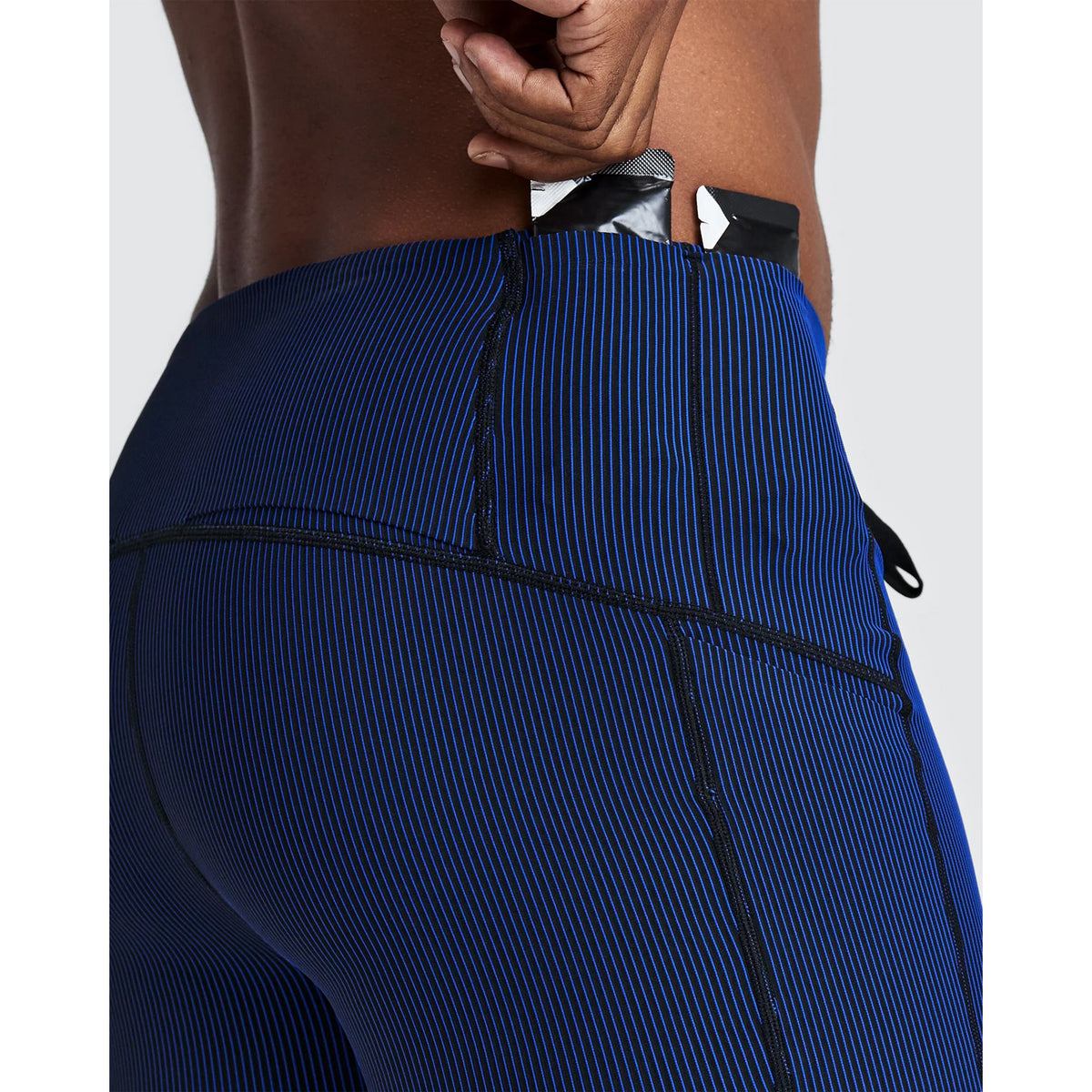 A person wearing Men’s Striped Cadence Half Tights Black / Bauhaus Blue with a small packet being placed into a waistband pocket.
