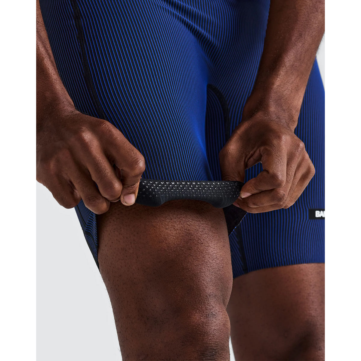 Hands pulling up the black and Bauhaus blue striped leg of Men’s Striped Cadence Half Tights to show the silicone grip lining on the inside.