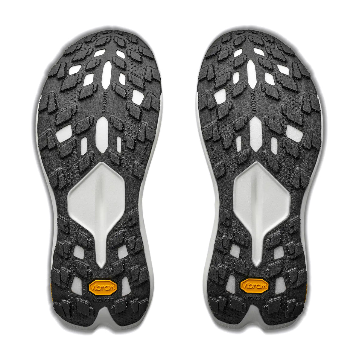 Two black and white Vibram outsoles, designed for the Men’s Tecton X 4 Trail Running Shoes by Hoka in Frost / Neon Tangerine, feature rugged tread patterns and yellow Vibram logos at the heels, displayed side by side on a white background.