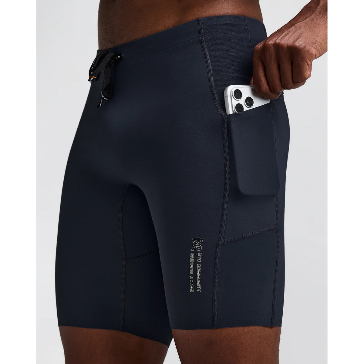 Person wearing dark athletic shorts, holding a smartphone partially inserted into a side pocket, with visible branding on the shorts near the thigh.