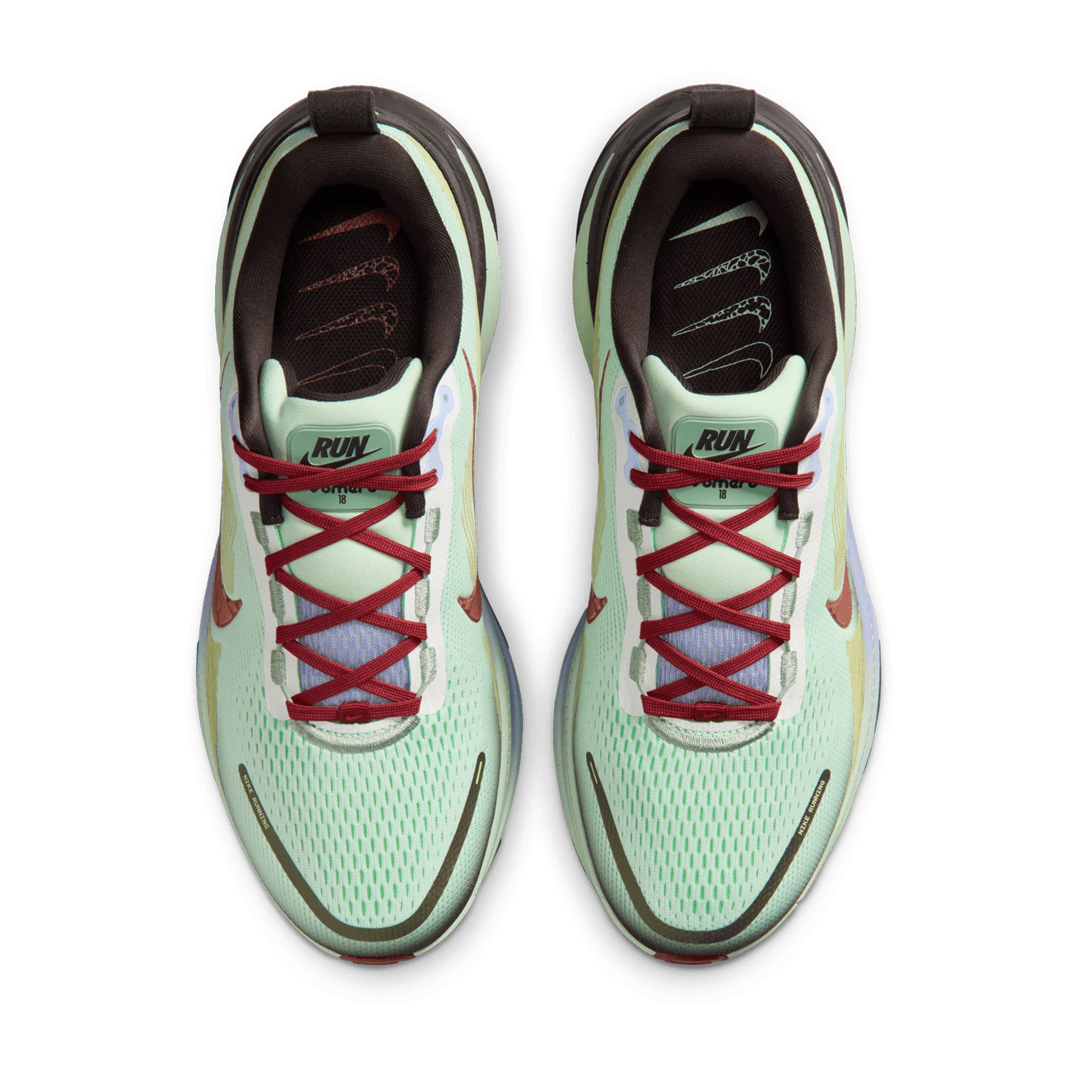 Top view of a pair of Nike Men’s Vomero 18 SE Running Shoes in Frosted Spruce, Tar, Purple Fade, and Rugged Orange. These road running shoes feature light green uppers with red laces, black lining, and red Nike swoosh logos. Designed for exceptional comfort with dual-density cushioning, the insoles are decorated with multiple white Nike swoosh graphics.