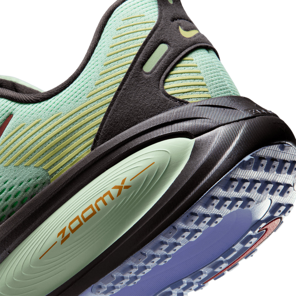 Close-up of the heel and sole of a green and black athletic shoe with yellow accents, showing textured grip and the word ZOOMX printed on the side.