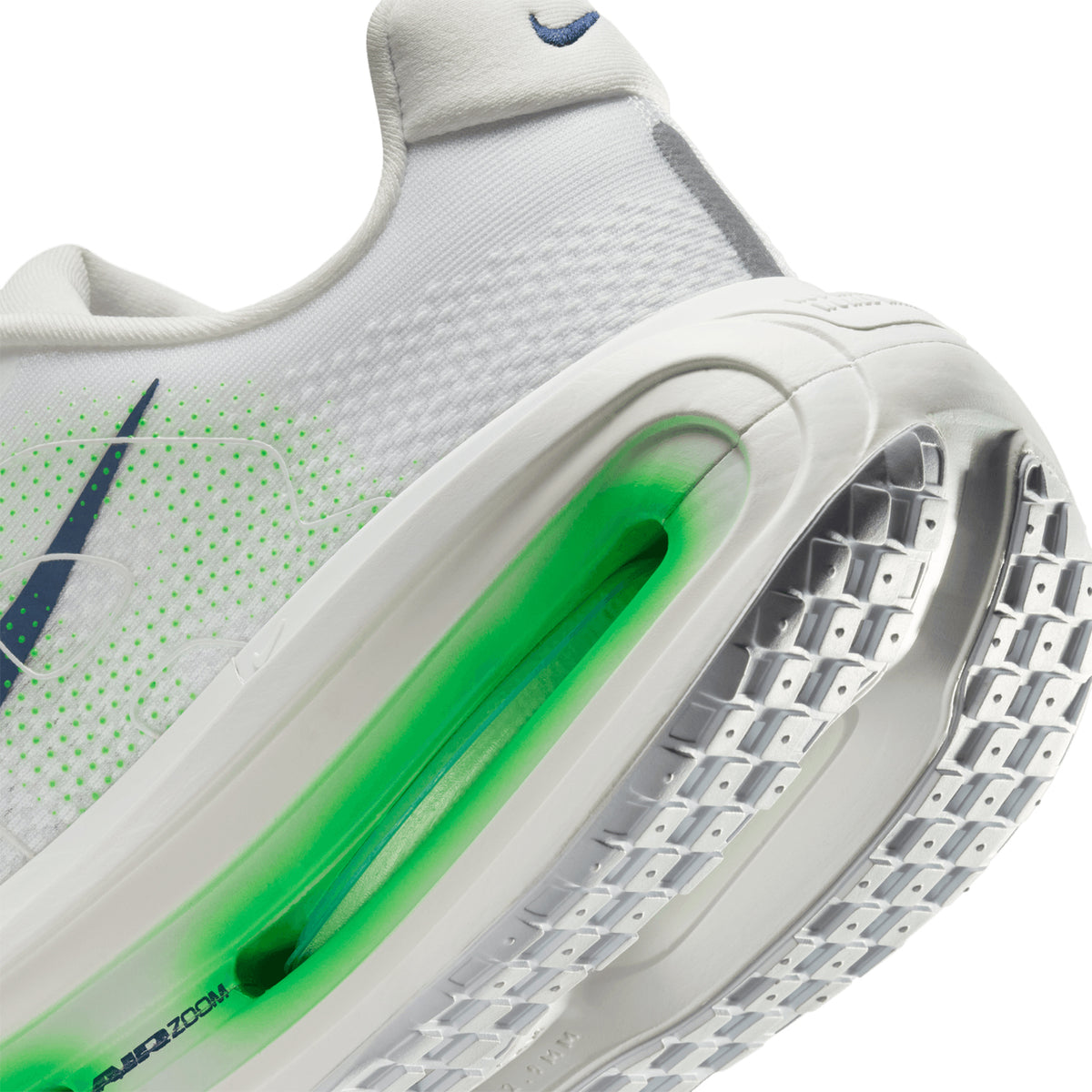 Close-up of a white athletic shoe, showing a green Air Zoom unit in the sole and textured tread pattern. A blue Nike swoosh logo is visible on the side.
