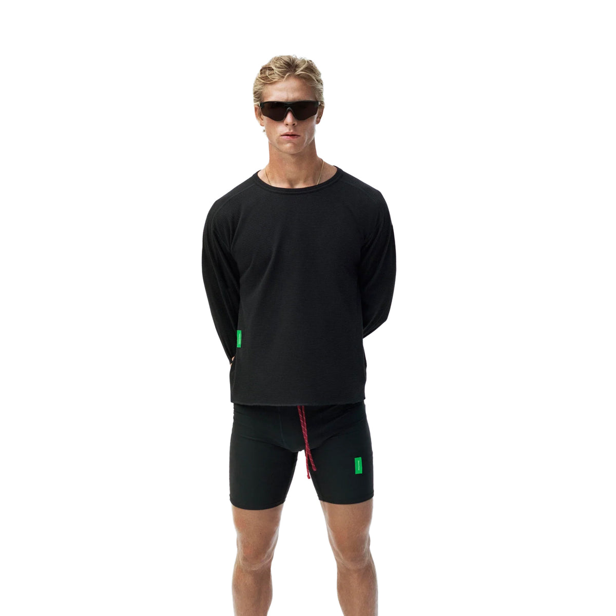 A person wearing a black District Vision Men’s Waffle Top Black long-sleeved shirt and black athletic shorts with sunglasses.