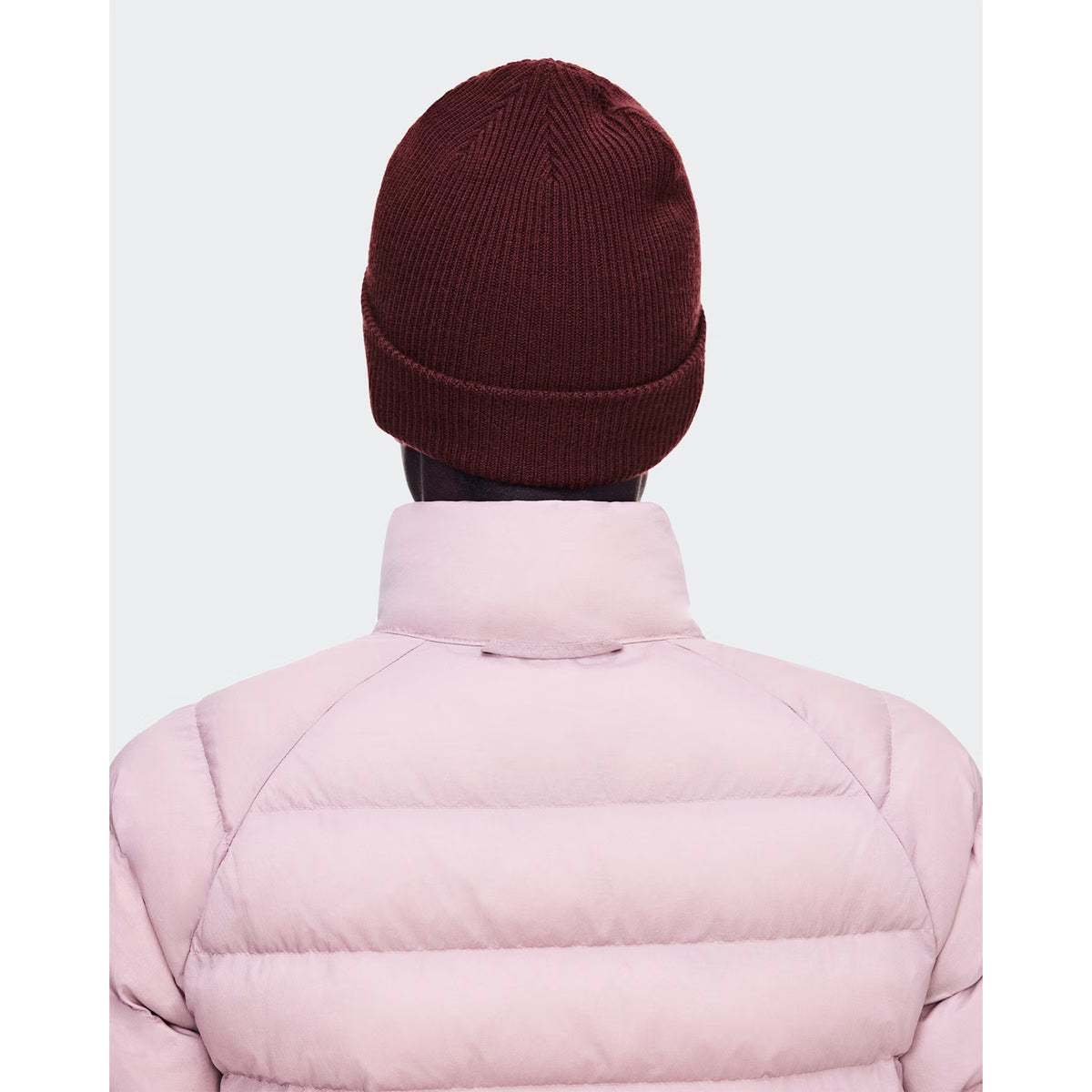 A person is seen from behind against a plain light background, wearing the On Merino Beanie Maroon—crafted for optimal temperature regulation on chilly days.