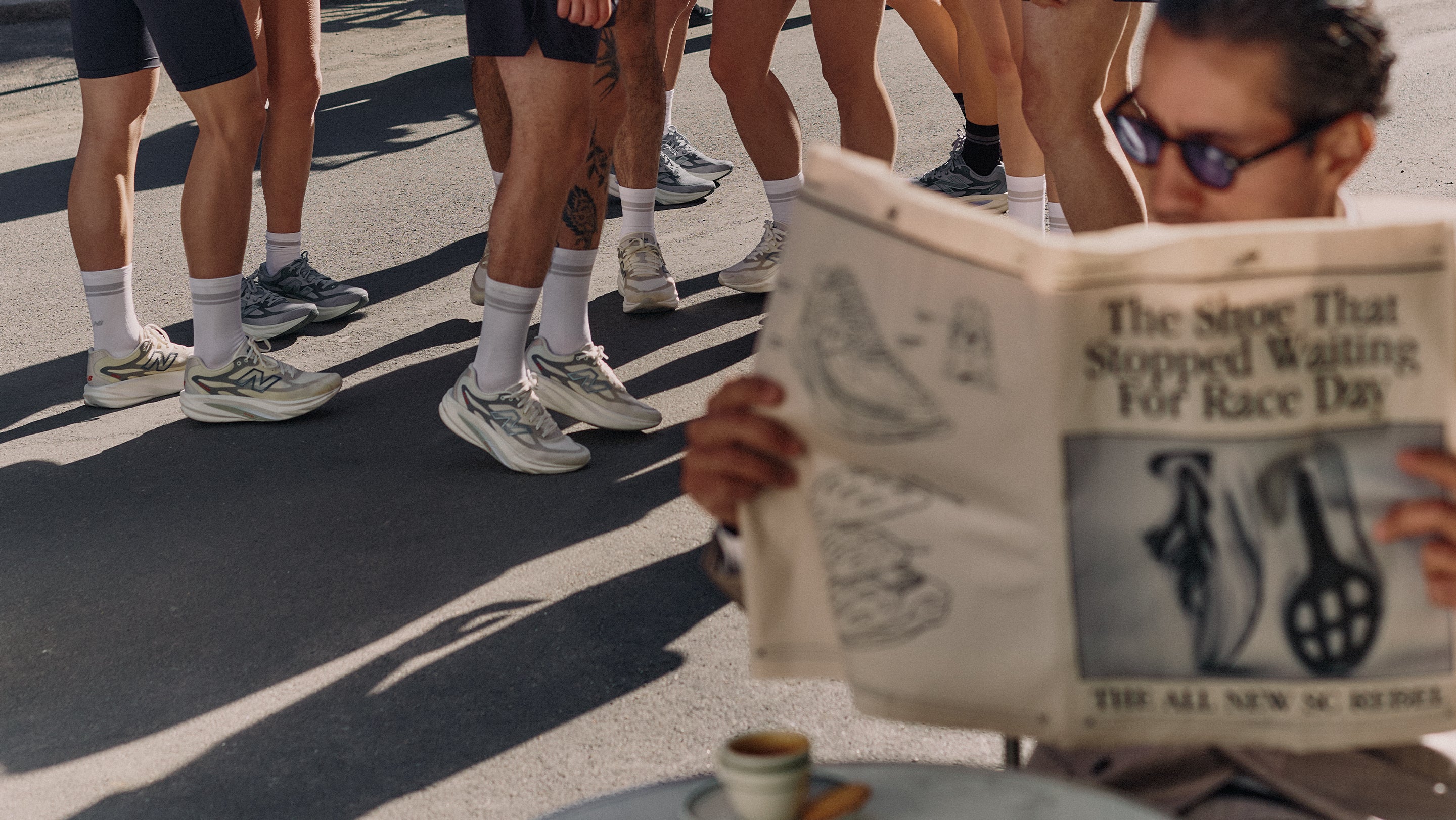 New Balance SuperComp Rebel campaign header showing group of runners wearing SuperComp Rebel shoes with white socks on sun-drenched tarmac alongside a man reading a newspaper headlined The Shoe That Stopped Waiting For Race Day