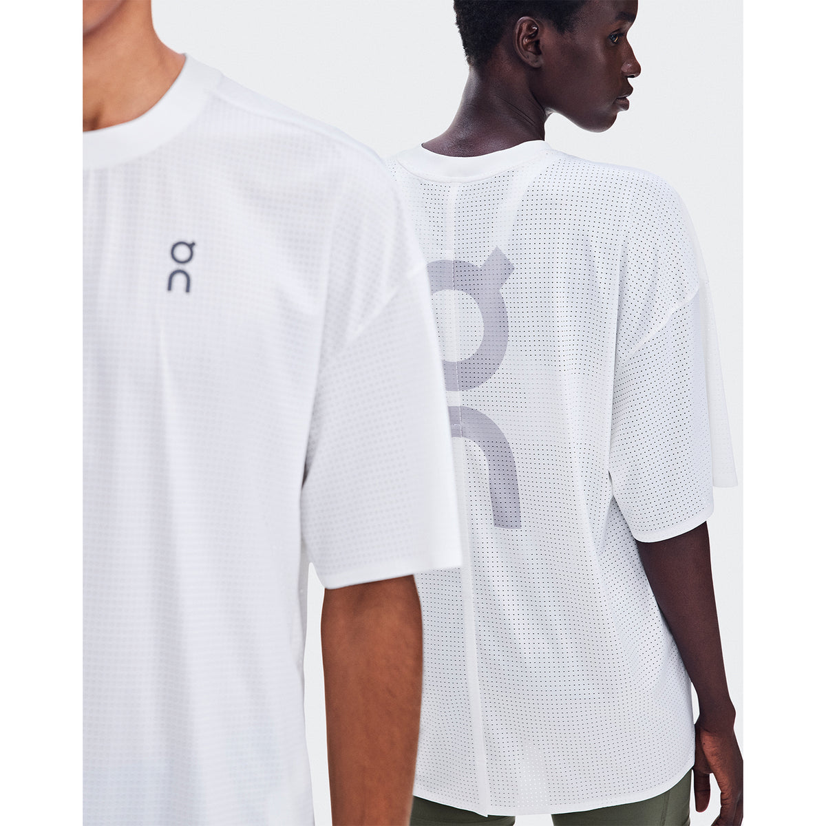 Two people wear the On Oversize Run-T LN1 White shirts, featuring an oversized running t-shirt design crafted from ultra-light, breathable mesh fabric. One model is partially visible facing forward, while the other turns away to display the logo printed on the back. Both are posed against a plain white background.