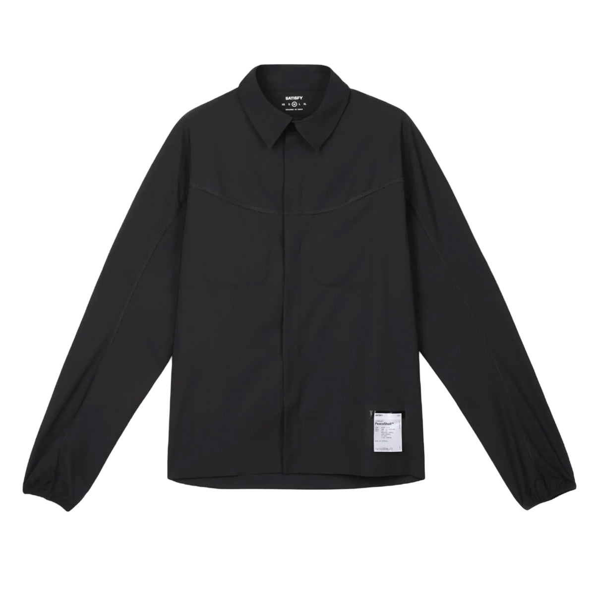The Satisfy PeaceShell River Shirt Black is a lightweight, long-sleeve button-up shirt with a collar, dual chest pockets, and a small white label near the bottom hem. It offers wind protection and is inspired by classic utility designs.