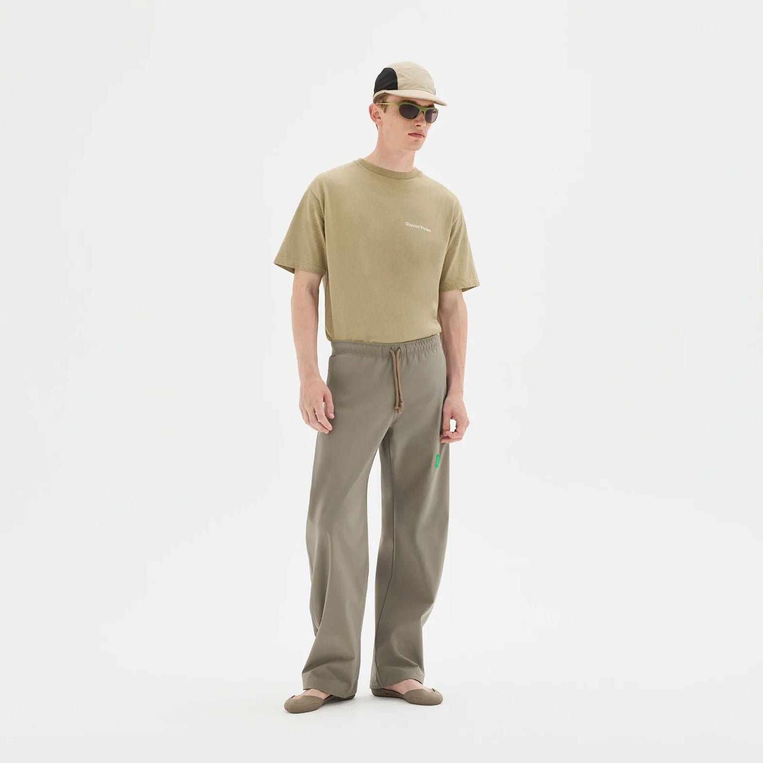 District Vision Performance Panelled Mesh Hat in Sand — full body view worn on model showing 3-inch brim profile, sand colourway and honeycomb mesh panel construction with running kit