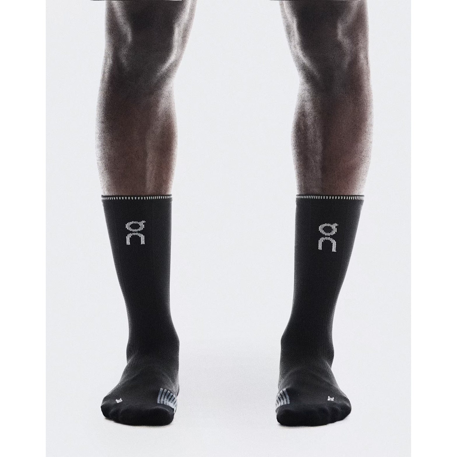 On Performance Run Sock High Black Eclipse front view on runner showing contrast logo and reflective yarn