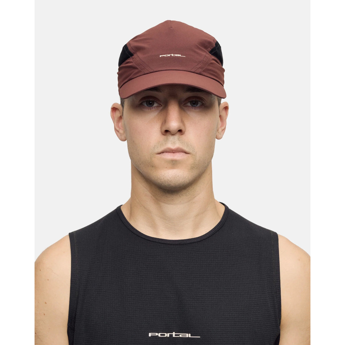 A person wearing the Portal Planar Lightweight Cap in Bitter Chocolate and a black sleeveless shirt stands against a plain white background, looking directly at the camera with a neutral expression.